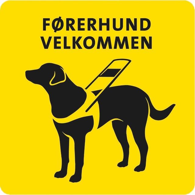 Klistremerke med teksten "Førerhund velkommen" og en sort/hvit tegning av en førerhund med sele