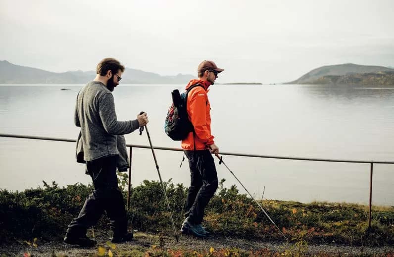 To personer går tur med staver langs en fjord.
