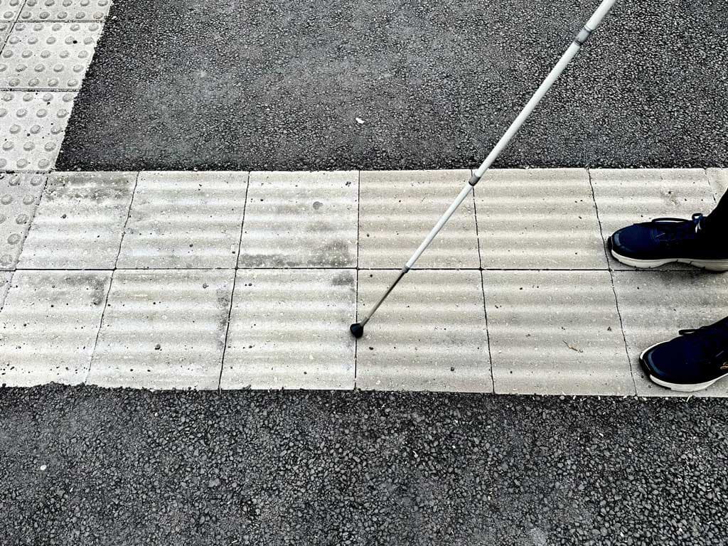 To ben og en mobilitistokk står på en ledelinge av betong. Sort asfalt rundt