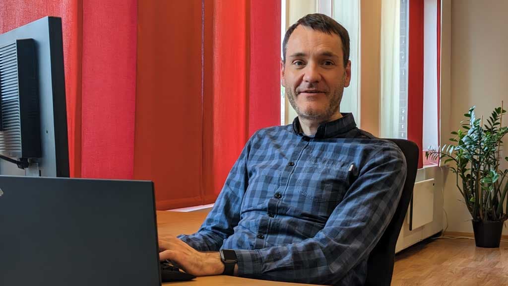 Generalsekretær i Norges Blindeforbund, Per Inge Bjerknes i rutete skjorte bak et skrivebord , med PC og skjerm på bordet.