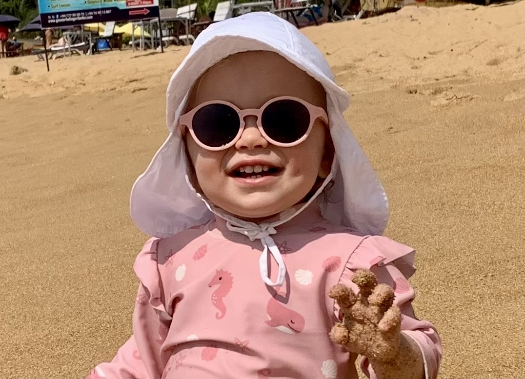 Et smilende barn med solbriller og solhatt på.