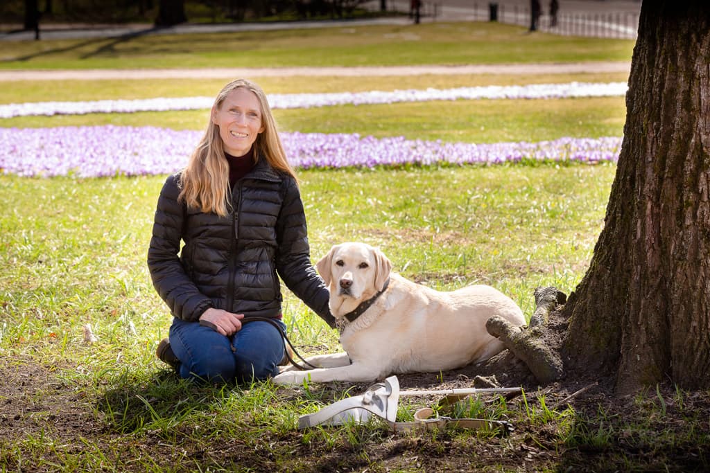 Åste sitter på kne ved siden av den lyse labradorførerhunden hennes Candy en vårdag i Slottsparken