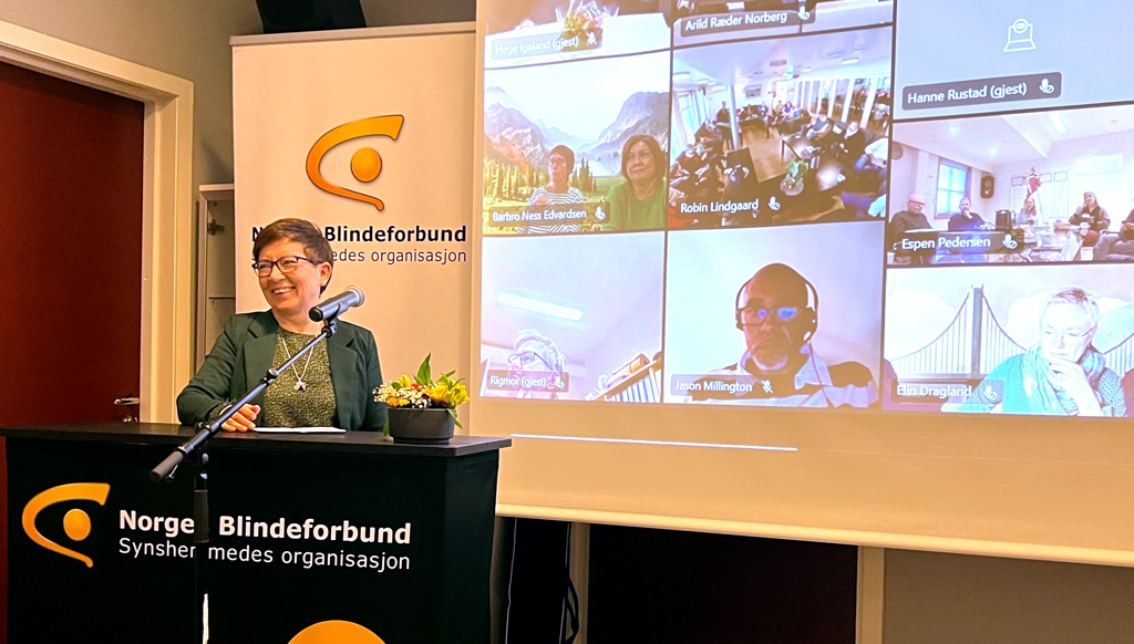 Berit Dalvik på talerstolen. Bak henne på storskjermen er det midnre bilder av deltagere i møtet fra forskjellige avdelinger rundt om i landet.