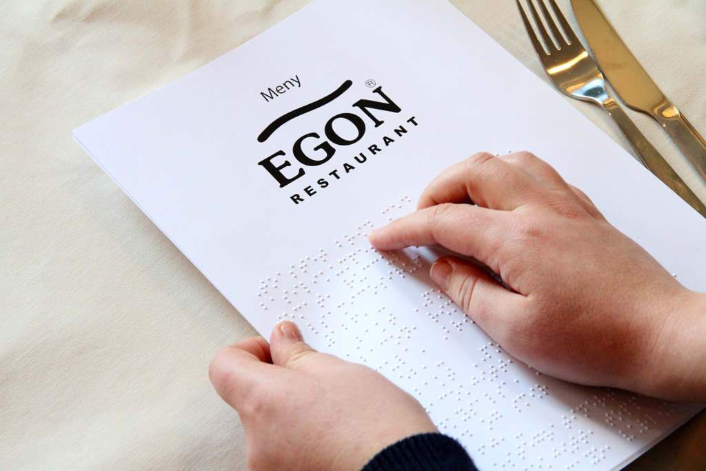 Bilde av hender som leser en EGON meny. Ved siden av menyen ligger det bestikk og det er hvit duk på bordet.