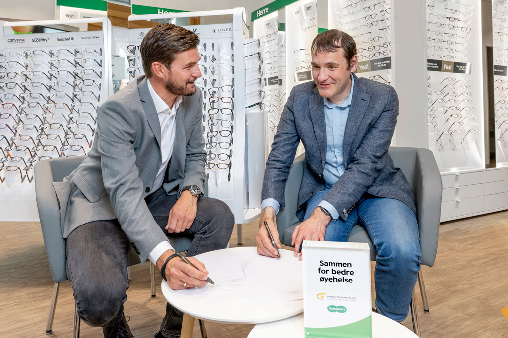 Specsavers-toppsjef, Henning Eriksen til venstre og generalsekretær Per Inge Bjerknes sitter i en brillebutikk og signerer på hver sin kontrakt.