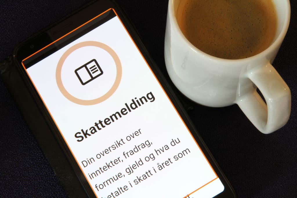 Deler av skattemeldingen synlig på en mobilskjerm. Ved siden av telefonen står det en kopp kaffe.