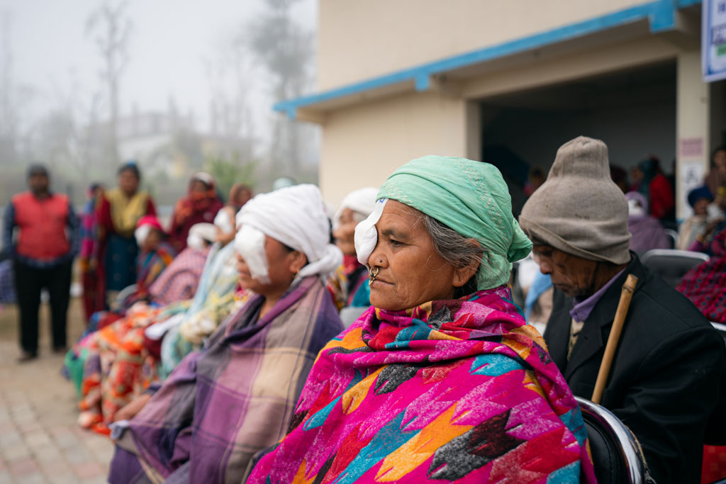 To kvinner sitter utendørs i fergerike klær med hver sin bandasje på ett av øynene.